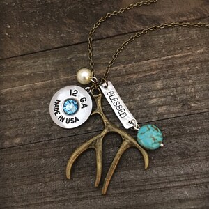 May include: A silver necklace with a 12 GA shotgun shell charm, a turquoise stone, a small antler charm, a pearl bead, and a silver tag that says "BLESSED".