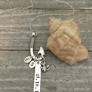 May include: Silver necklace with a fishing hook charm, a small turtle charm, and a charm with the letters 'E' and 'S'. The necklace also has a silver tag with the date '01.18.16' engraved on it.