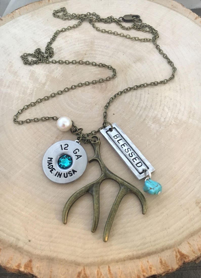 May include: A silver necklace with a 12 GA shotgun shell charm, a turquoise stone, a small pearl, and a silver charm that says "Blessed". The necklace also features a bronze antler charm.