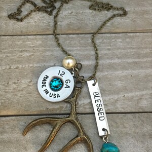 May include: A necklace with a silver bullet casing charm, a turquoise stone, a small antler charm, a pearl bead, and a silver tag that says "BLESSED".