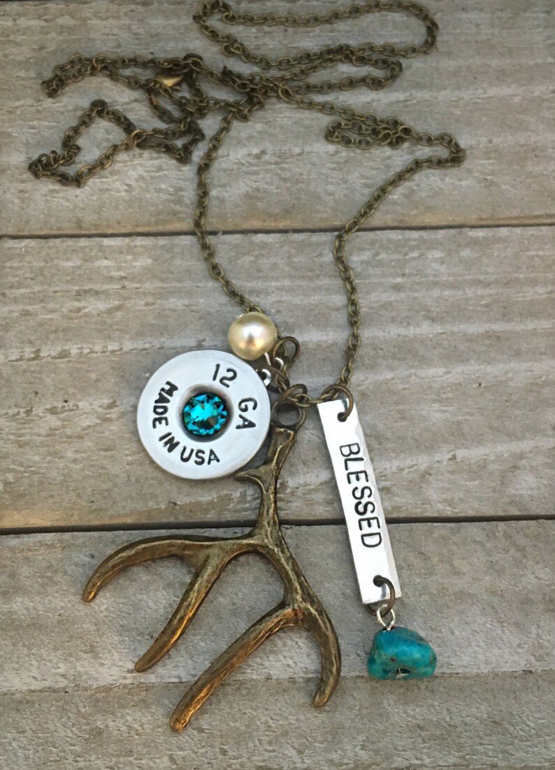 May include: A necklace with a silver bullet casing charm, a turquoise stone, a small antler charm, a pearl bead, and a silver tag that says "BLESSED".