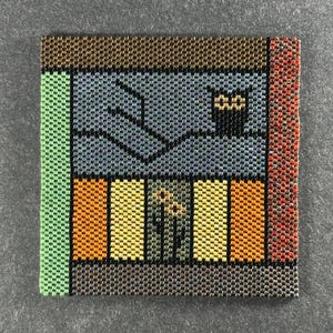 May include: Square beaded artwork depicting a stylized scene. The artwork features a window with a cat in a pot, and a row of colorful rectangles below. The color palette includes green, brown, orange, yellow, and gray.
