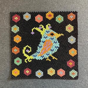 Könnte beinhalten: Ein quadratisches, mit Perlen besetztes Kunstwerk mit einem bunten Vogeldesign auf schwarzem Hintergrund. Der Vogel hat blaue, orangefarbene und gelbe Details. Der Rand ist mit kleinen, bunten blütenartigen Formen verziert. Wahrscheinlich ein Untersetzer oder ein dekoratives Stück.