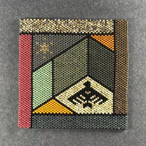 May include: Square beaded artwork with a geometric design. The piece features a variety of colors, including red, green, yellow, and brown, arranged in a mosaic pattern. A black border frames the design, and the beads create a textured surface.