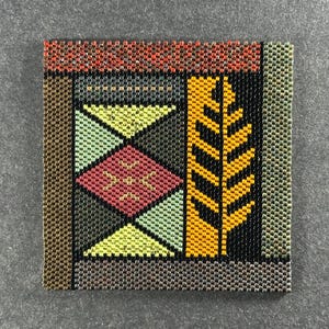 May include: Square beaded artwork with a geometric design. The piece features a border of brown and gray beads, with sections of red, yellow, green, and black beads. The central design includes triangles, diamonds, and a leaf-like pattern.