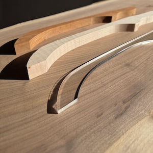May include: Three wooden and acrylic curved handles, two are wood and one is clear acrylic. The handles are on a wooden surface.