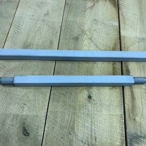 May include: Two metal rods, one longer than the other, are painted a light gray color. The rods are lying on a wooden surface.