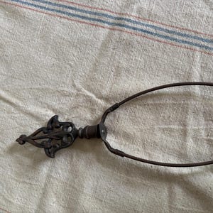 May include: An antique metal object with a decorative, ornate finial and a circular handle. The metal has a dark, aged appearance, suggesting it is vintage. The object is likely a tool or decorative item.