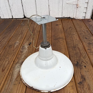 May include: A vintage white metal industrial light fixture with a circular shade and a silver pole. The fixture has a square mounting plate and visible wiring. The shade has some rust around the edges.