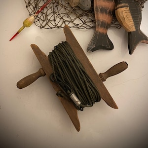 May include: A rustic nautical-themed arrangement featuring a wooden spool of green rope, a fishing net, and three carved wooden fish in shades of gray, brown, and black. A red and yellow fishing bobber is also present.