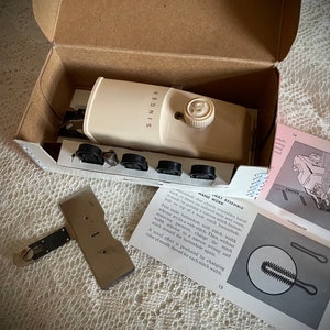 May include: Vintage Singer sewing machine in its original box. The off-white machine has a dial and the Singer logo. Accessories and instruction manual are included. The box is open, revealing the contents.