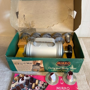 May include: Vintage Mirro Cooky and Pastry Press set in its original box. The set includes a silver aluminum press with various shaped cookie cutters and nozzles. The box is green and tan with the text "15 Fancy Shapes So Easy To Make".