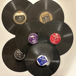 May include: A collection of vintage vinyl records with various label designs. The records are black with colorful labels, including Brunswick, Columbia, and Diamond. The labels feature text and graphics.