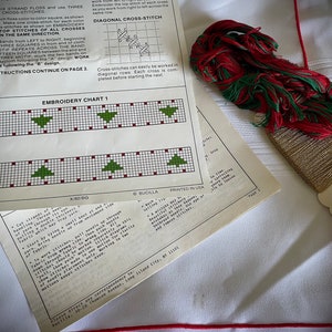 K&ouml;nnte beinhalten: Kreuzstich-Stickset mit Anleitungen und Diagrammen. Enth&auml;lt ein Blatt mit einem Weihnachtsbaum-Muster, rotes und gr&uuml;nes Stickgarn und wei&szlig;en Stoff mit rotem Rand. Das Set ist zum Basteln.