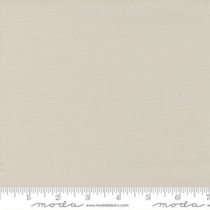 May include: A solid, off-white fabric with a subtle texture. The fabric is shown with a ruler for scale.