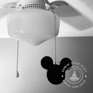 May include: Black and white image of a ceiling fan pull chain with a Mickey Mouse shaped pull. The pull has the text "Sawin' Pixie Dust Magical Home Decor" around it.
