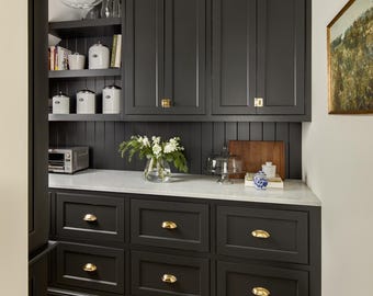 May include: A black pantry with white countertops and gold hardware. The pantry has upper cabinets, open shelves, and lower drawers. There is a small appliance on the counter and a decorative glass cloche.