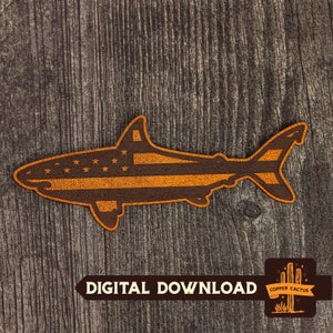 Pode incluir: Uma silhueta de tubarão de couro marrom com um design de bandeira americana. O tubarão está em um fundo de madeira com o texto "DOWNLOAD DIGITAL" e um logotipo para "COPPER CACTUS".