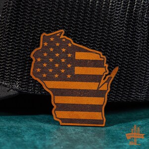 May include: A brown leather patch shaped like the state of Wisconsin with the American flag design. The patch is on a black background.