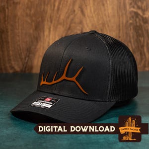 May include: Black and brown trucker hat with a brown elk antler design. The hat has a black mesh back and a black front panel. The hat is adjustable.