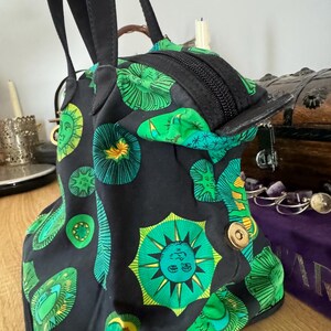 May include: A black tote bag with green and yellow sun and star designs. The bag has two black handles and a zipper closure.