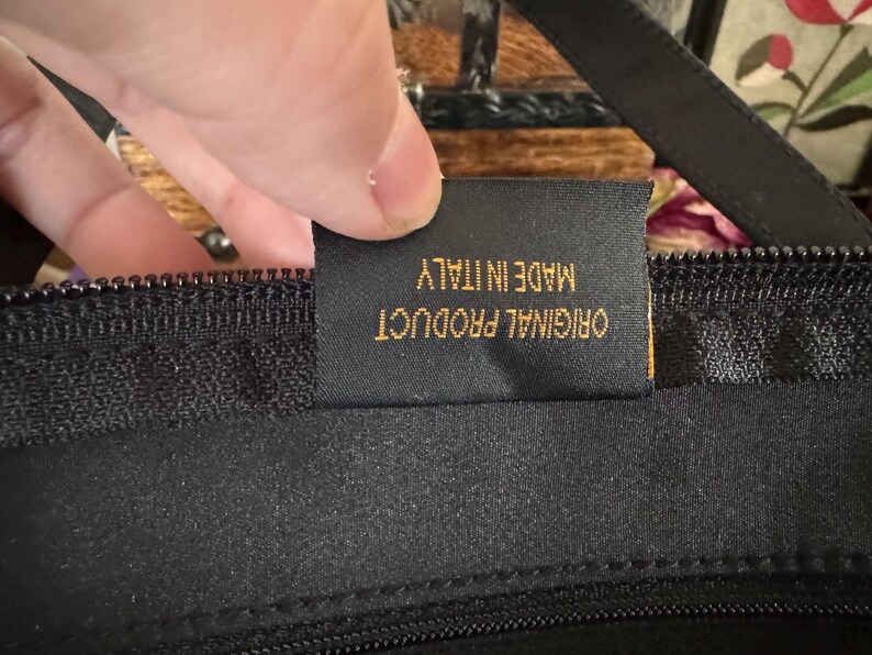 May include: Close-up of a black zipper with a gold tag that reads "ORIGINAL PRODUCT MADE IN ITALY".