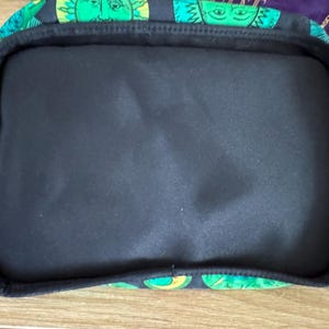 May include: A black fabric tote bag with a green and yellow pattern of faces. The bag has a black lining and a zipper closure.