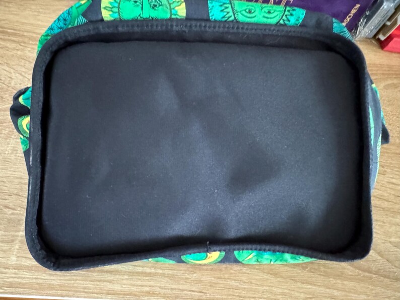 May include: A black fabric tote bag with a green and yellow pattern of faces. The bag has a black lining and a zipper closure.