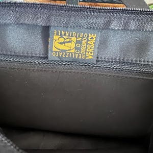 May include: A black bag with a gold label that reads "VERSACE REALIZZATO  CO.M.  DISEGNO ORIGINALE".