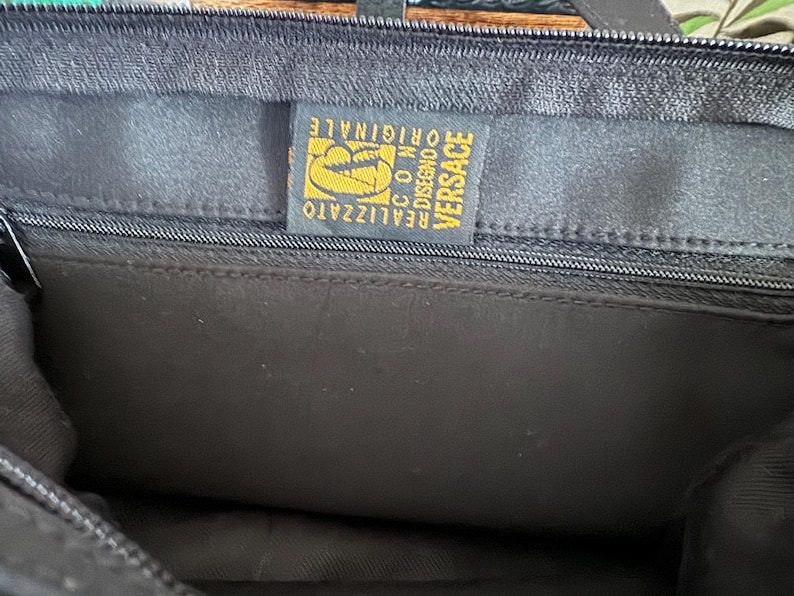 May include: A black bag with a gold label that reads "VERSACE REALIZZATO  CO.M.  DISEGNO ORIGINALE".