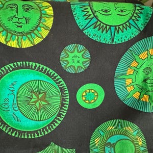 May include: Black fabric with a repeating pattern of green, yellow, and blue suns and moons. The suns have faces and the moons have crescent shapes.