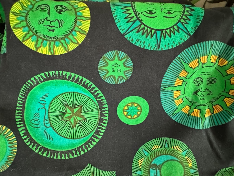 May include: Black fabric with a repeating pattern of green, yellow, and blue suns and moons. The suns have faces and the moons have crescent shapes.