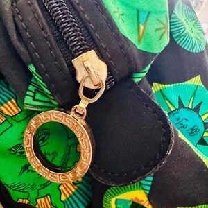 May include: A black zippered bag with a green and yellow patterned fabric. The zipper has a gold charm with a circular design.