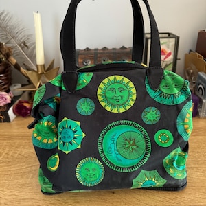 May include: A black tote bag with green and yellow sun and moon designs. The bag has two black handles.