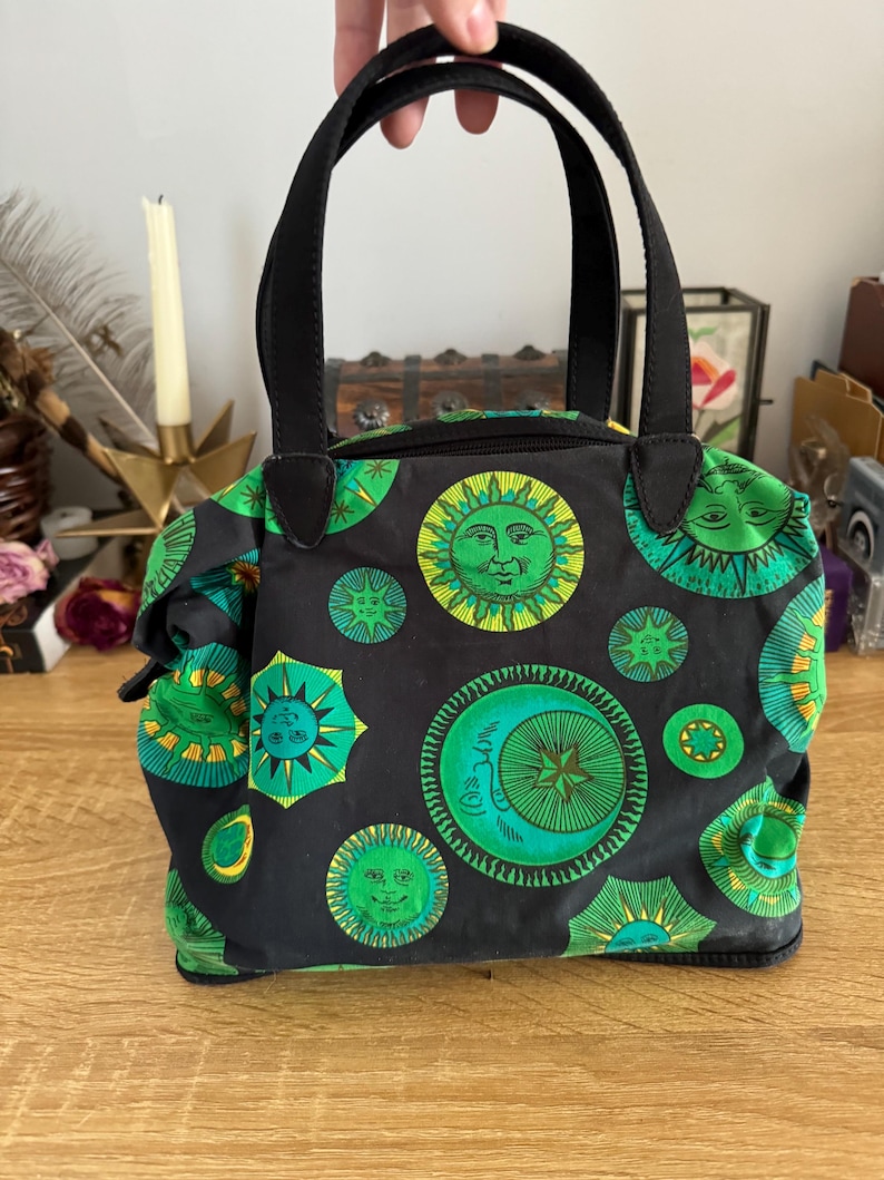May include: A black tote bag with green and yellow sun and moon designs. The bag has two black handles.