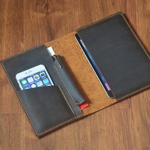 May include: A dark brown leather portfolio with a yellow stitch detail. The portfolio is open and has a phone, pen, and cards inside.