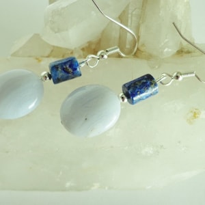 May include: Silver earrings with blue and gray gemstone beads. The earrings feature a silver hook closure.