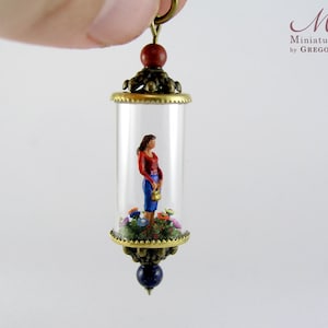 Miniature world pendant. Woman standing in a garden of colorful flowers and bushes.
