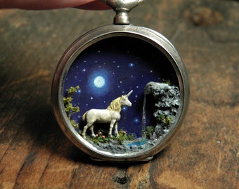 Miniature magical scene inside antique silver pocket watch showing a unicorn standing next to a waterfall in a natural environment