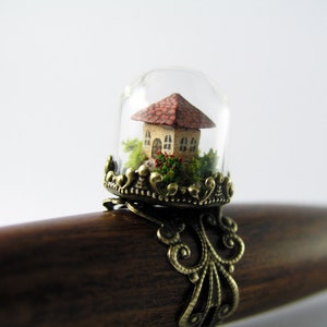 Miniature world. Tiny little house amidst garden in a glass dome ring.