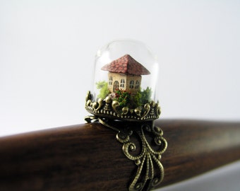 Miniature world. Tiny little house amidst garden in a glass dome ring.