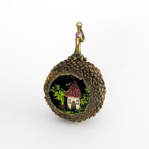 Miniature world pendant. Tiny house amidst trees and flowering bushes in real acorn.