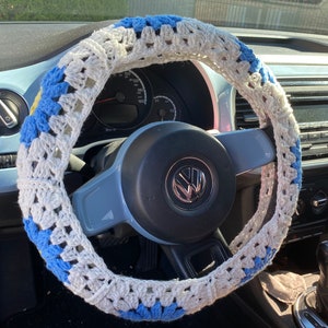 May include: A white and blue crocheted steering wheel cover. The cover is made with a simple stitch pattern and has a blue and white color scheme.