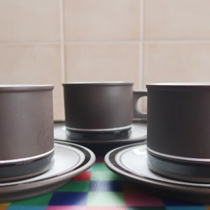 May include: Three brown ceramic teacups with white bands and matching saucers. The cups have a simple design and are perfect for a classic afternoon tea.