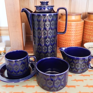May include: A ceramic coffee set featuring a tall coffee pot with a lid, a creamer, and a cup with a saucer, all decorated in a deep blue and dark grey geometric pattern. The set includes a matching open bowl, all displaying a consistent repeating motif.