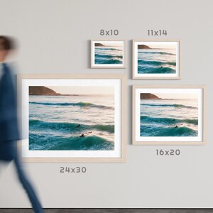 May include: Framed art prints of a coastal scene with surfers in the ocean. The prints are displayed in various sizes: 8x10, 11x14, 16x20, and 24x30 inches. The text "Size Guide (inches)" is visible.