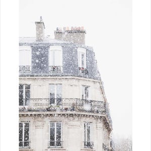 May include: A photograph of a Parisian building in a snowstorm. The building has a light-coloured facade with multiple windows and balconies. The roof is a dark grey colour. Snowflakes are falling, creating a winter scene.