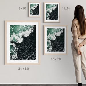 Op de afbeelding: Een collectie ingelijste kunstdrukken met een luchtfoto van oceaangolven. De prints worden in verschillende formaten getoond, waaronder 20x25 cm, 28x35 cm, 40x50 cm en 61x76 cm, met een licht houten frame. Het kunstwerk toont tinten groen en wit.