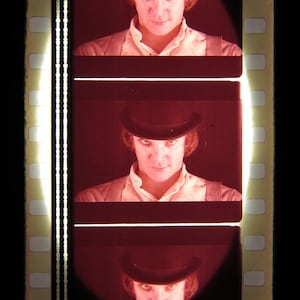 May include: A film strip with three frames showing a person wearing a black bowler hat and a white shirt. The person's face is visible in each frame.