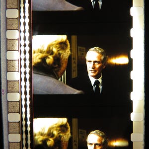 Könnte beinhalten: Filmstreifen mit drei Bildern eines Mannes in Anzug und Krawatte, der einem anderen Mann mit blonden Haaren gegenübersteht. Der Mann im Anzug hat helles Haar und blickt nach vorne. Der Filmstreifen hat rechteckige Perforationen am Rand.